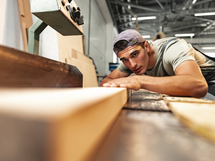 Giovane falegname concentrato mentre lavora un asse di legno con un macchinario professionale in un laboratorio artigiano.