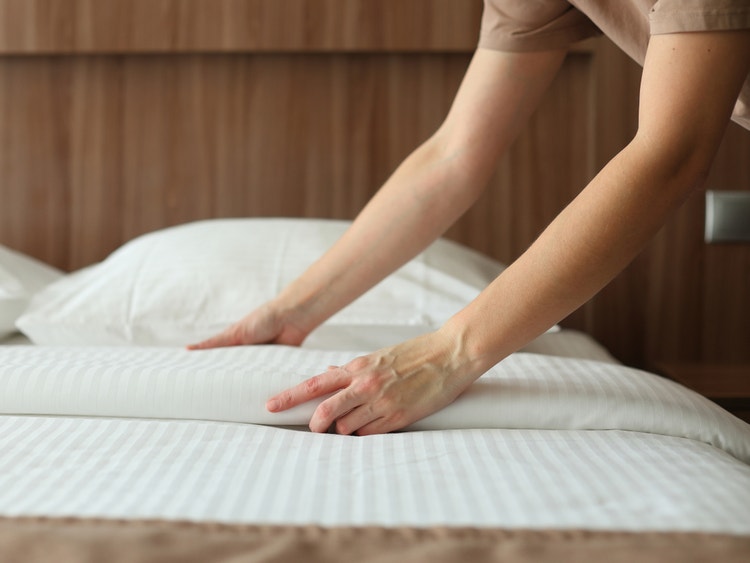 Dettaglio delle mani di un addetto alle pulizie mentre rifà con cura un letto in una camera d&#39;albergo.