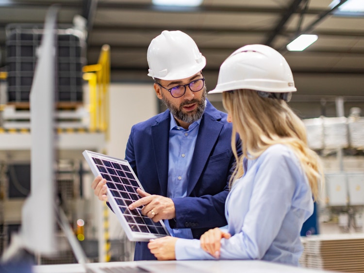 Due ingegneri con caschetto bianco esaminano un piccolo pannello solare all&#39;interno di un moderno stabilimento industriale.