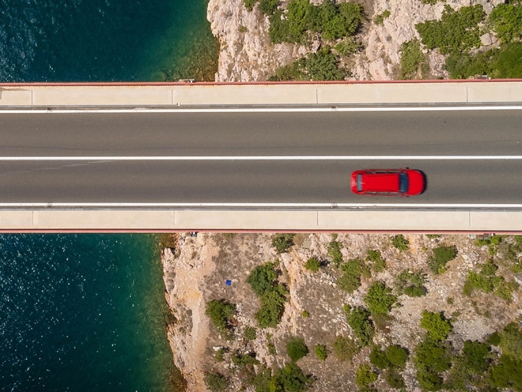 Auto rossa che percorre una strada costiera vista dall’alto