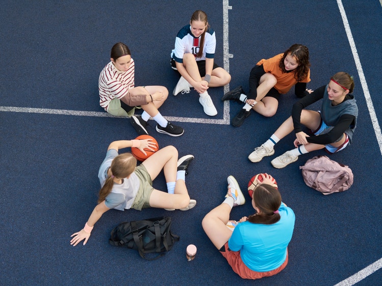 Veduta dall&#39;alto di un gruppo di ragazze sedute in cerchio su un campo da basket blu con dei palloni.