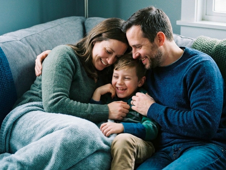 Una famiglia felice con un bambino si abbraccia affettuosamente seduta sul divano di casa.