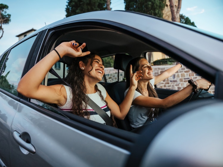 Due ragazze sorridenti e felici viaggiano in auto, cantando durante un viaggio su strada.