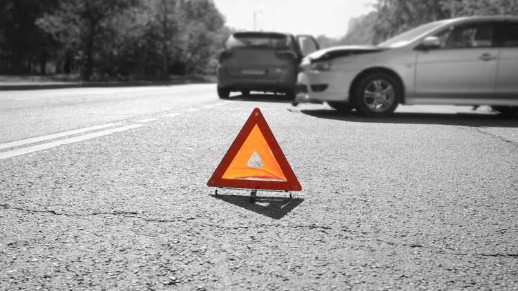 Triangolo di emergenza su strada con due auto incidentate sullo sfondo