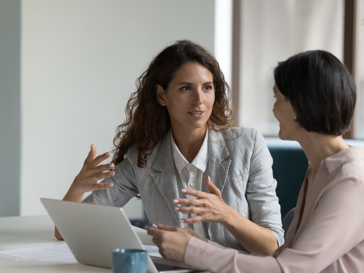 Una consulente in giacca a righe parla con una cliente davanti a un laptop in ufficio moderno.