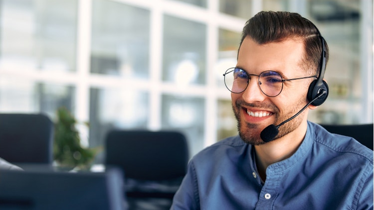 Operator di customer care sorridente con occhiali e cuffia con microfono lavora in ufficio.