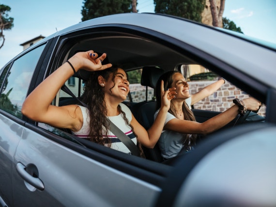 Due ragazze sorridenti e felici viaggiano in auto, cantando durante un viaggio su strada.