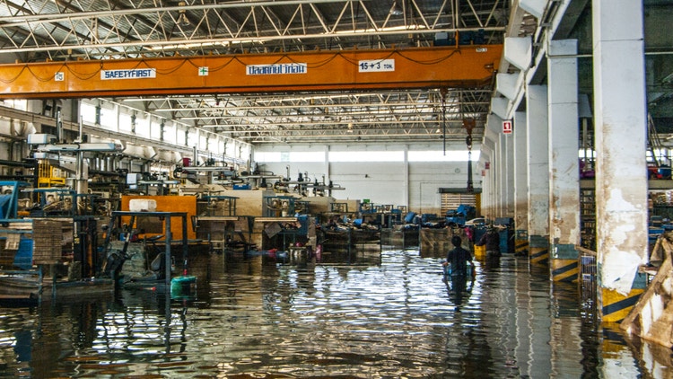 Interno di una fabbrica allagata con macchinari industriali sommersi dall&#39;acqua e due persone in lontananza.